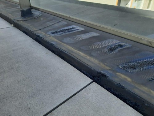 Poškození PVC fólie kolem skleněného zábradlí na terase bytového domu